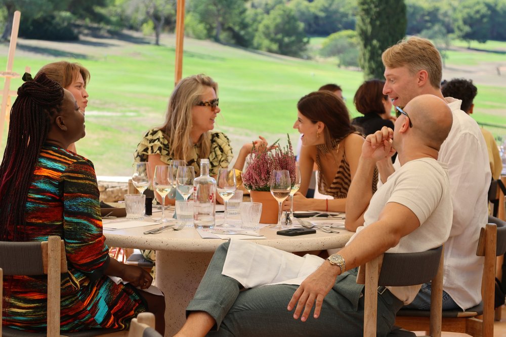 Guests in conversation around a round table outdoors, wine glasses on the table.