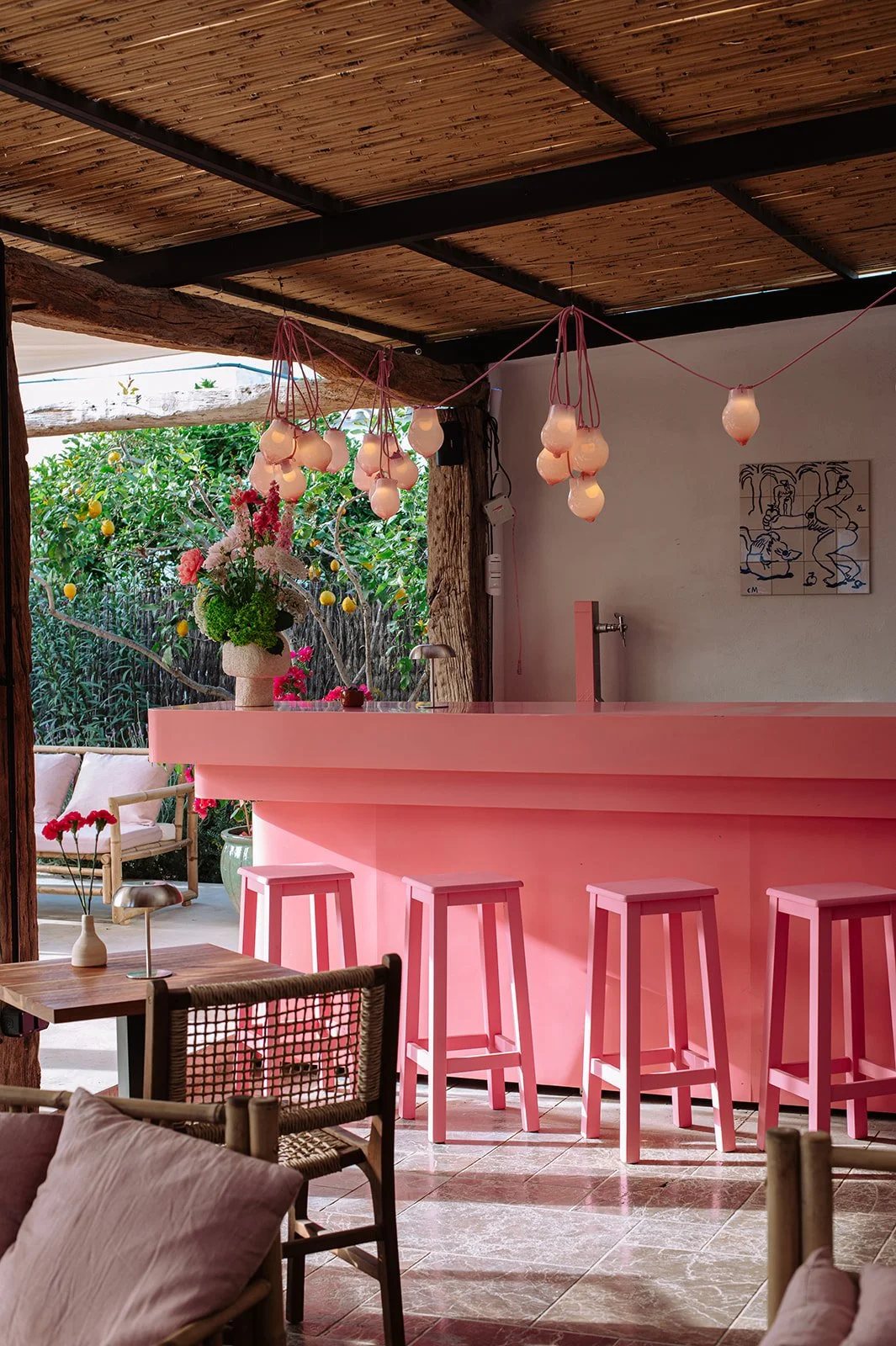 The pink bar at Mira Cocktail Lounge in Sant Miquel, with pink stools, glass lamp lights and flowers, and the garden terrace beyond.