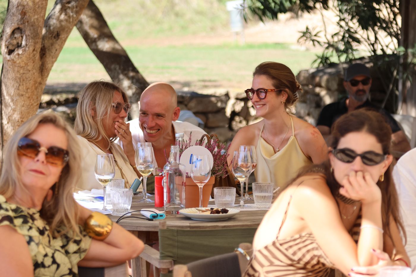 Friends laughing together around a lunch table in the shade.