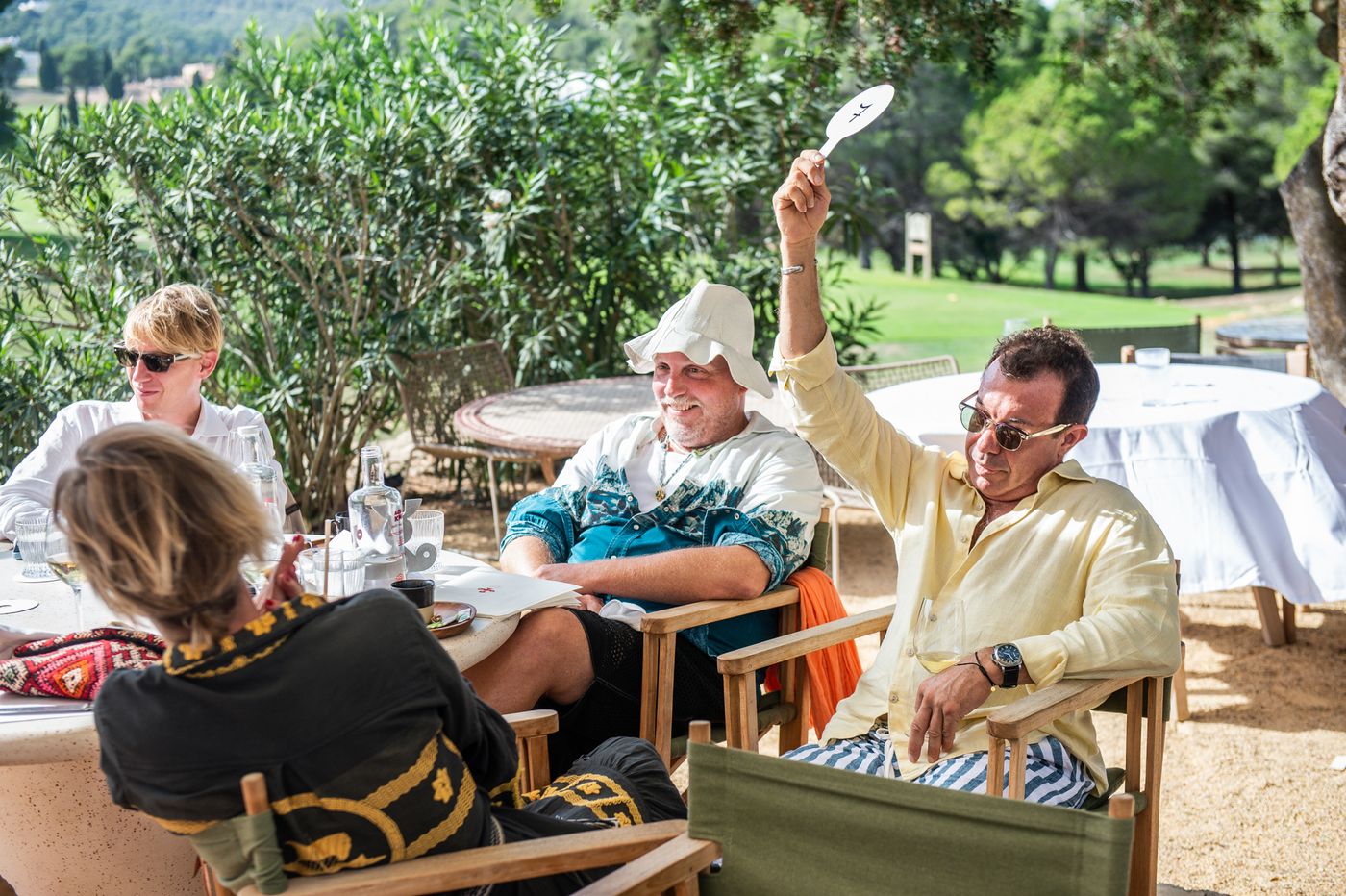 A guest in a pale yellow jacket raises a paddle to bid.